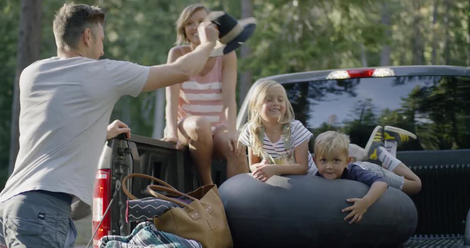 Man playfully putting a cowboy hat on his daughter as she sits in the back of a pickup with her mom and brother
