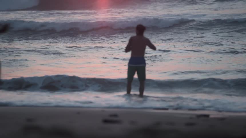Man taking photographs of waves crashing onto beach at sunset
