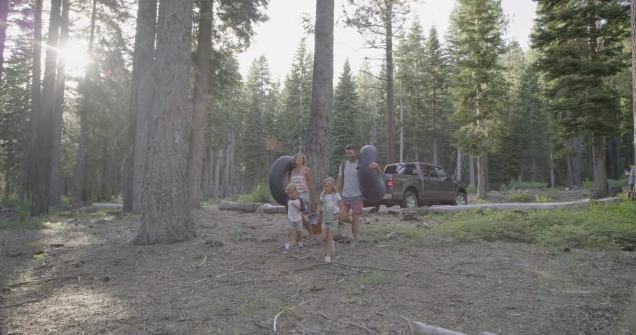Parents carry tire inner tubes as they walk with their children in a natural setting in summer