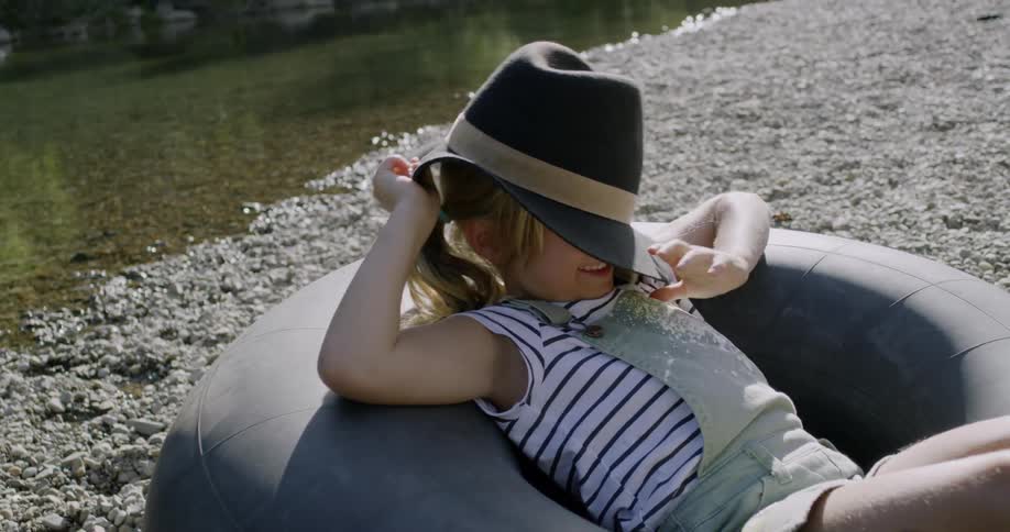 A child puts on a hat as she lays in the inner tube