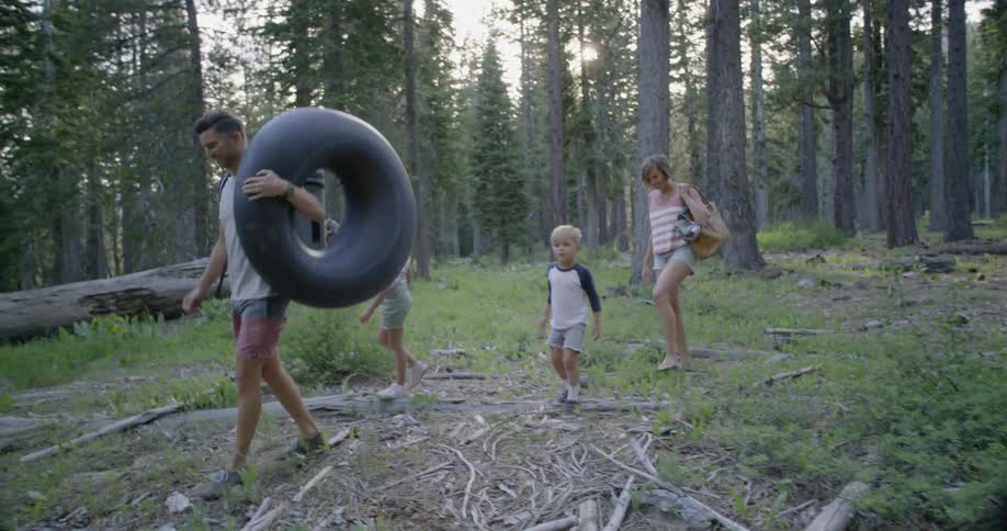 A father is carrying a tire inner tube as he walks with his family in a natural setting