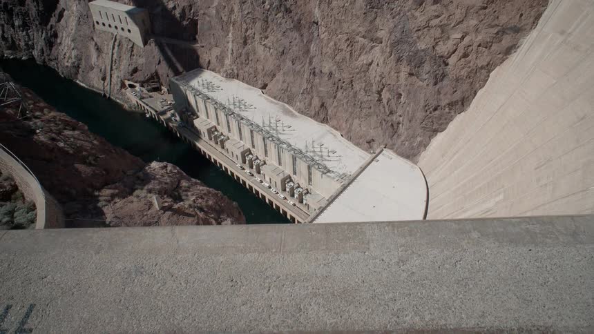 A dam is towering above a river and ravine in daylight