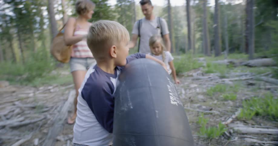 A boy is trying to carry a tire inner tube as his family walks in a natural setting