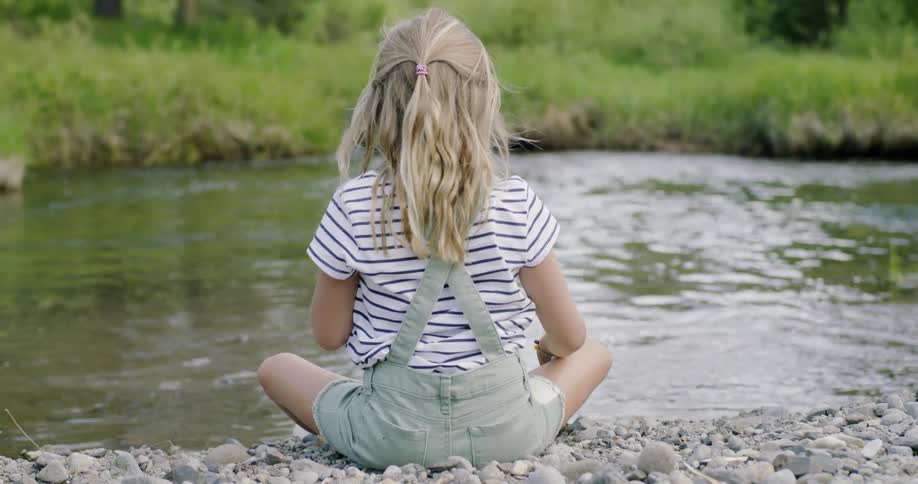 A girl sits on the rocks by the pond