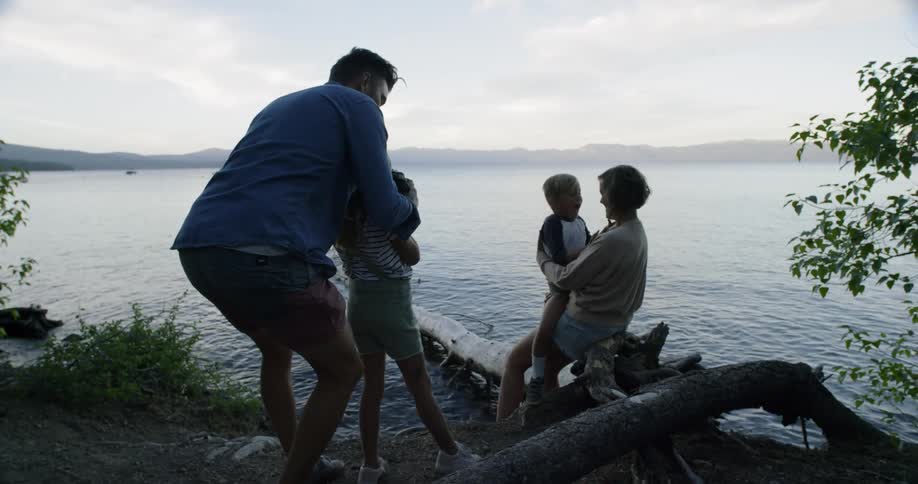 A father is helping his daughter take a lakeside photo of her mother and brother