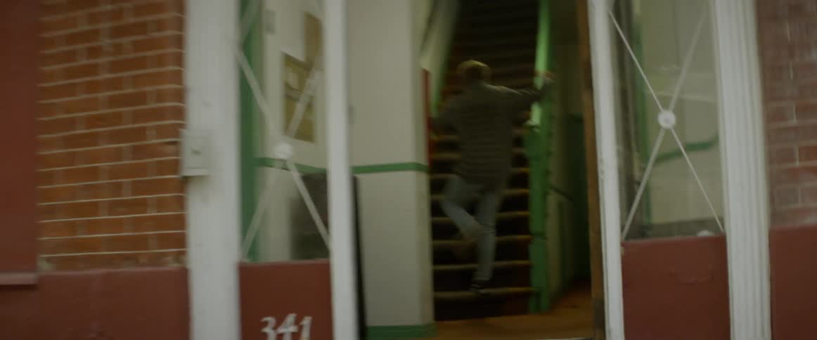 Man runs and almost falls then runs into a house up some stairs