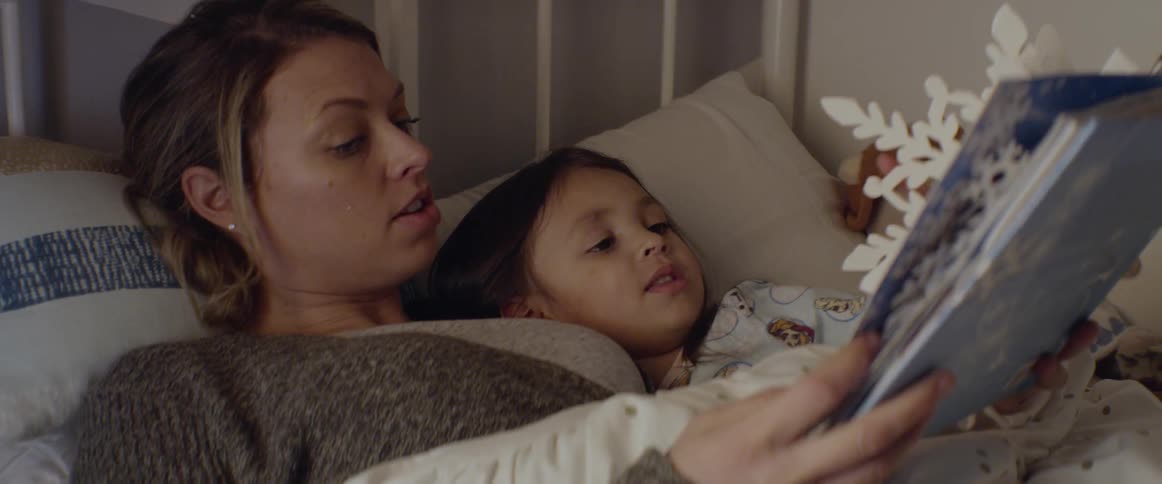 A mom reads a book to her daughter in bed