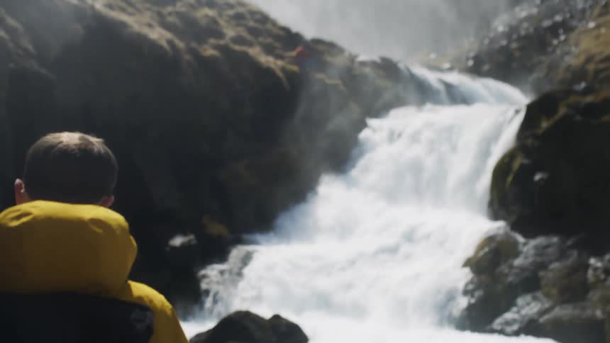 A man hiking near a waterfall is taking off his cap