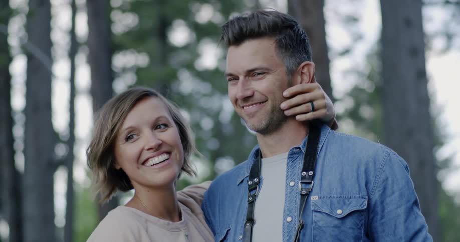 Smiling man and woman pose together in the woods