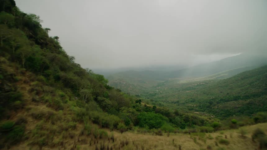 The sun is peeking through rain clouds in a mountain valley