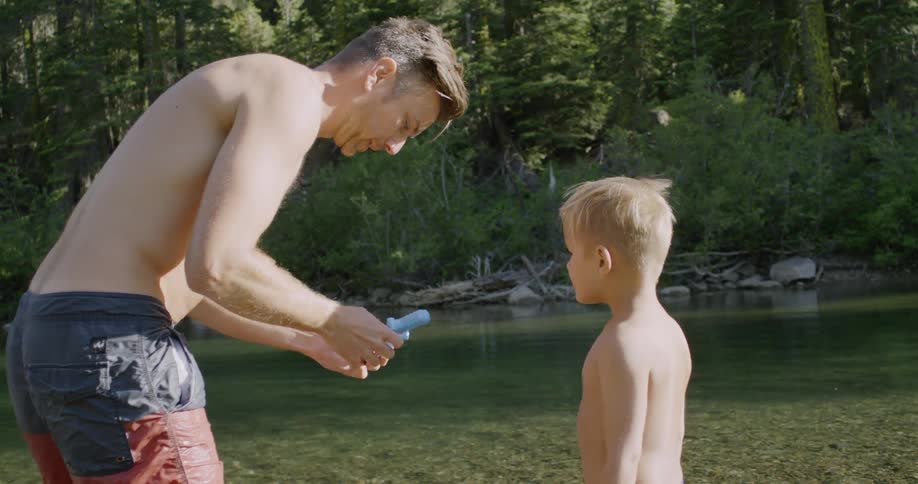 A man is helping his son with something next to a creek