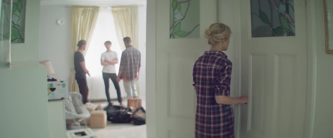 A woman looks at a group of men talking then opens the house door