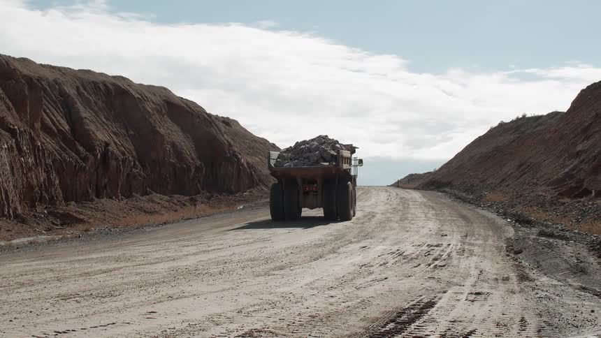 A dump truck is making its way over a dirt road on a cloudy day