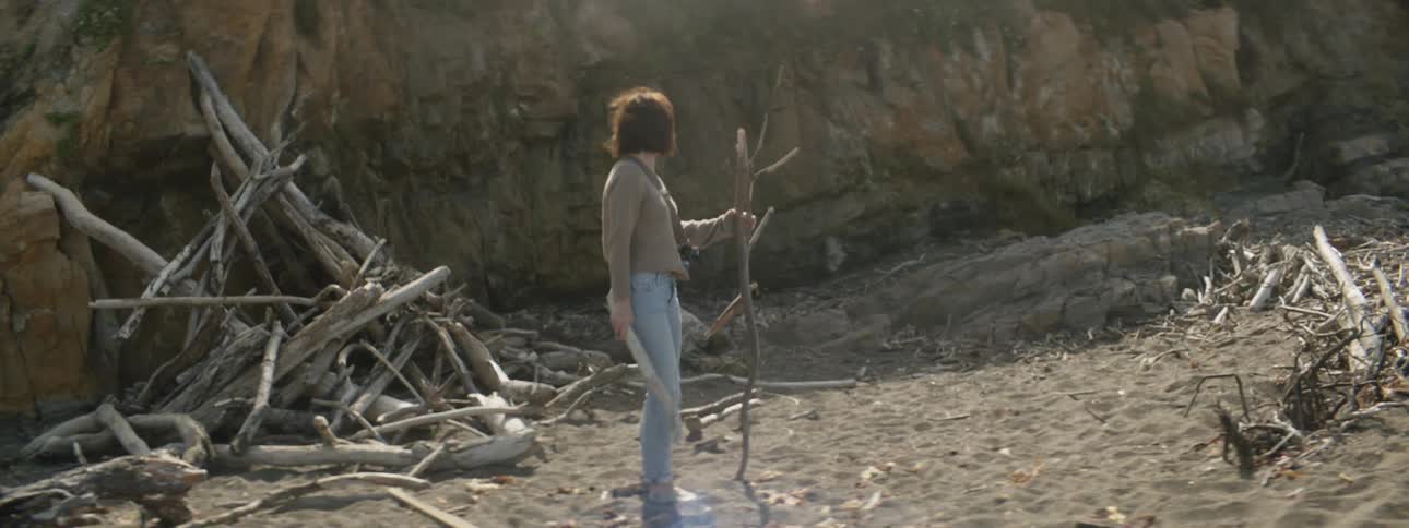 Woman is gathering sticks on sandy beach