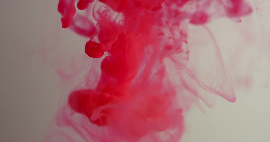 Red dye is falling into and spreading out in a liquid solution