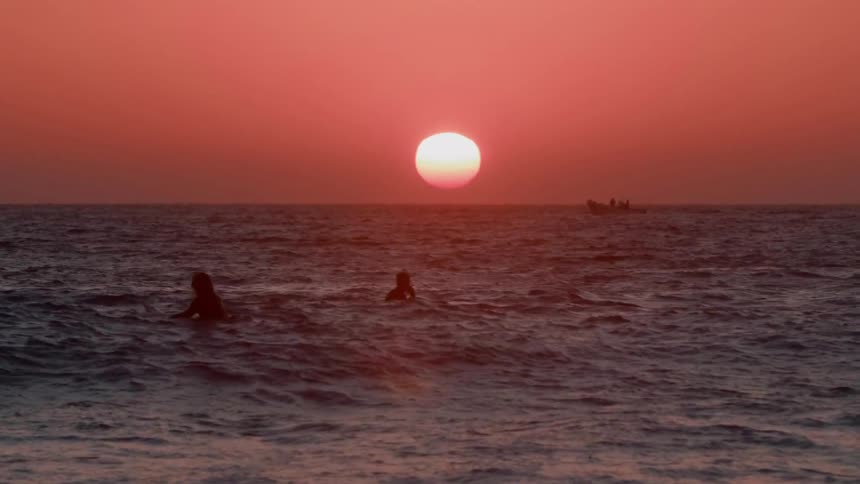 Two men floating on surfboards in ocean waves as sun sets