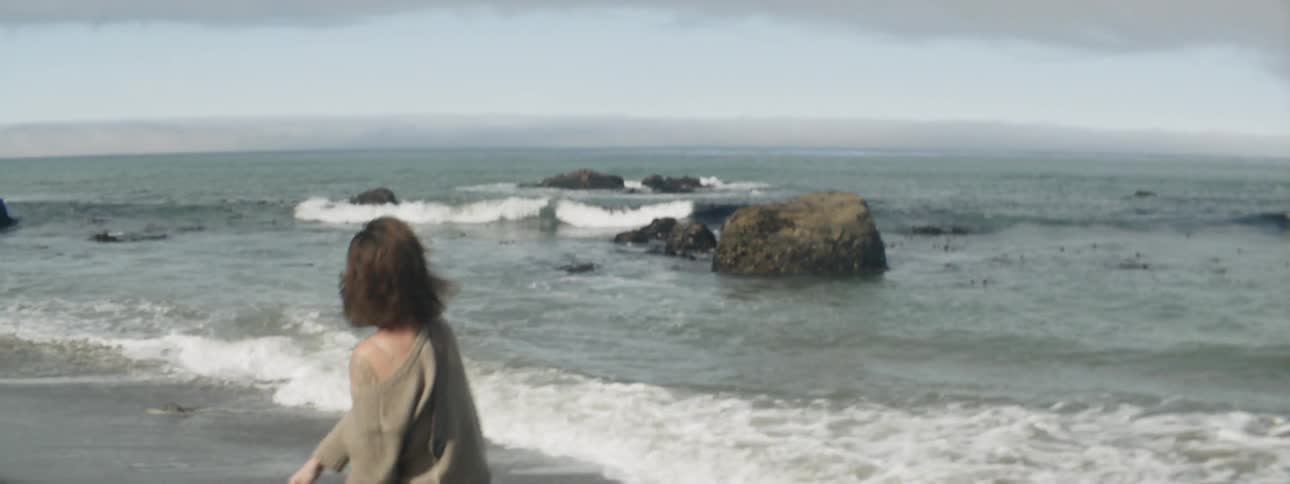 A woman is throwing stones into the ocean on a cloudy day