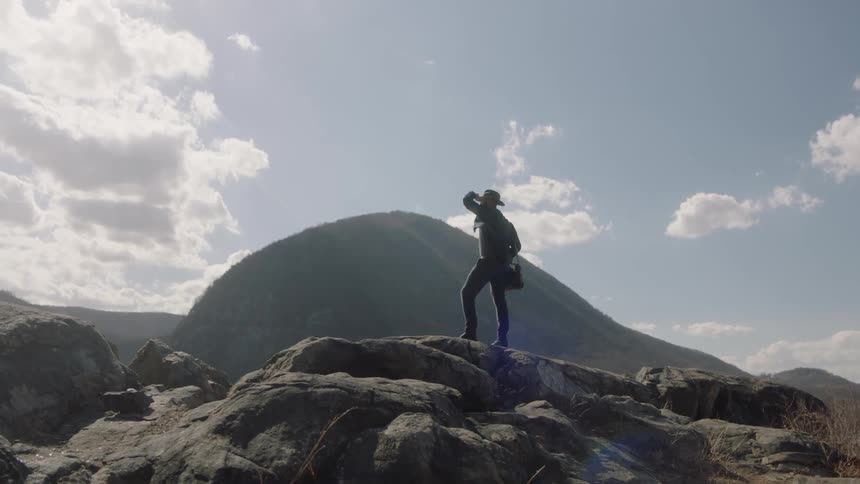 Man stands on a rocky hill shielding his eyes from the sunlight