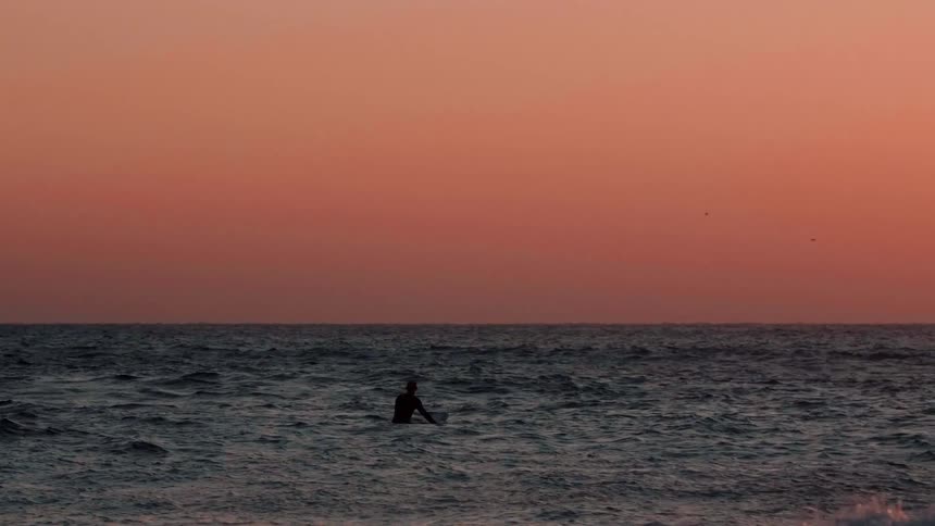 A man rides on his surfboard in the water at dawn