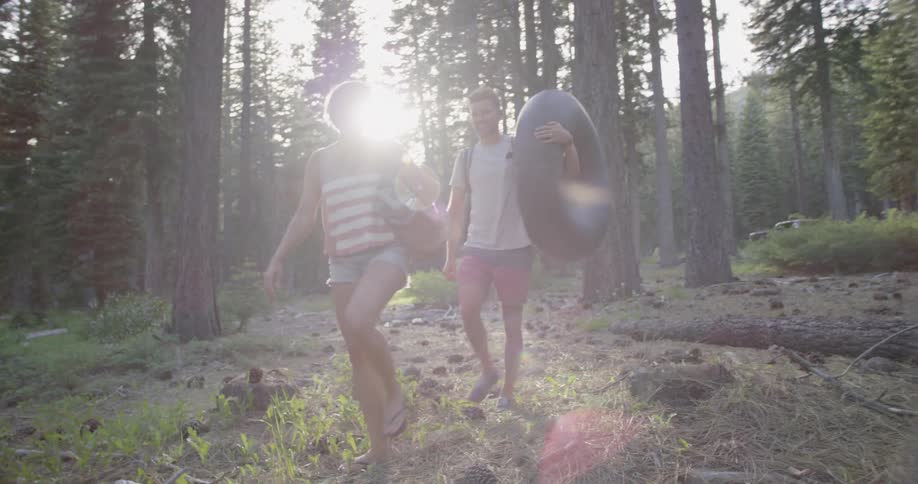 Woman carries a backpack and man carries a tube through the woods on  a sunny day