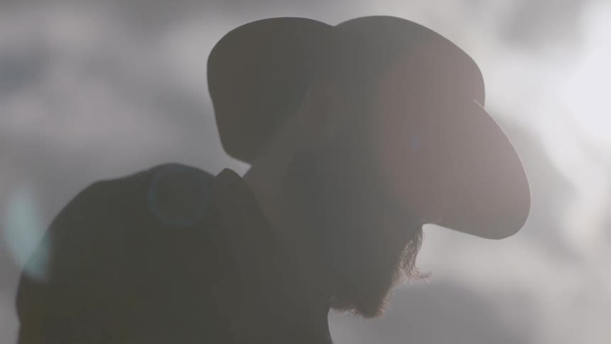 A man in a hat stands outside under the sun