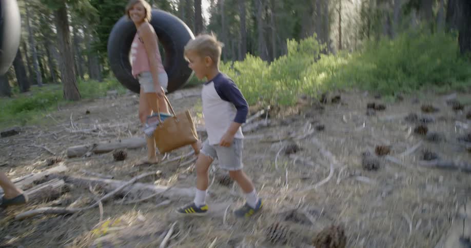 Family in a woodsy area walking around and the dad and mom have large inner tubes on their shoulders