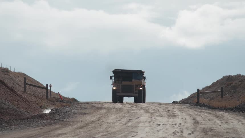 A dump truck is making its way over a dirt road on a cloudy day