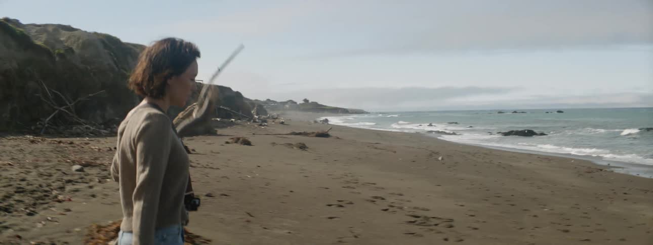 Woman wearing camera is walking with stick on beach