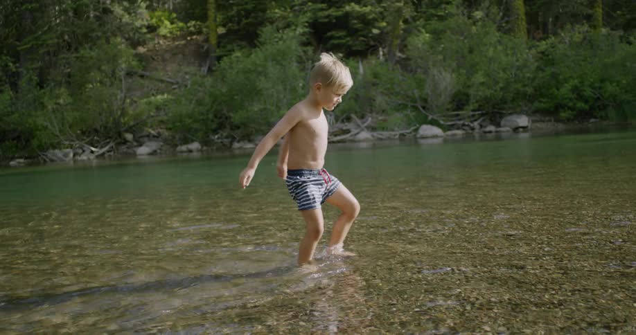 Little boy wades through shallow river water on sunny day