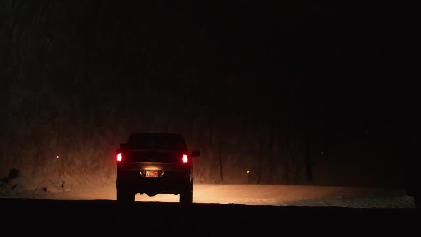 A pickup truck is driving on a dirt road in a desert landscape at night