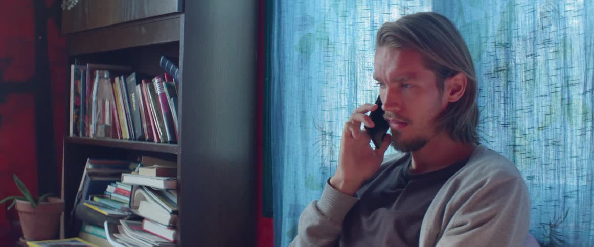 A man is inside a home talking to on a cell phone in daylight