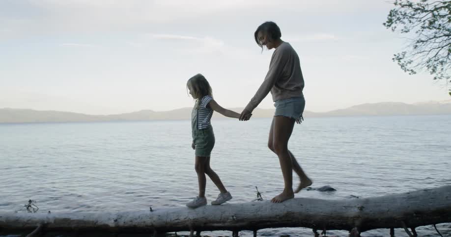 A mother and daughter are walking out over a body of water on a fallen tree in daylight