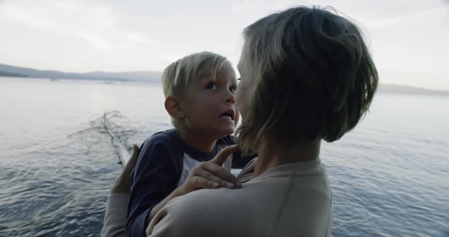 A woman holds her son as he makes faces and laughs