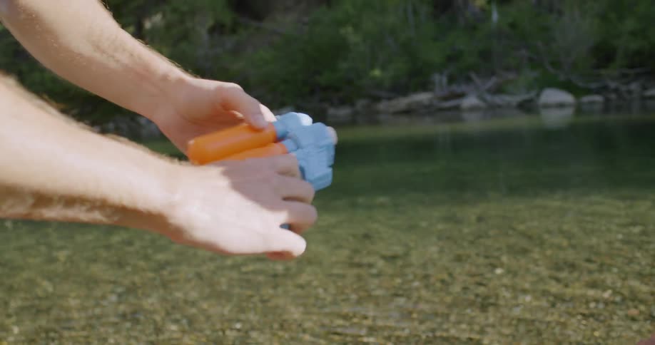 Father hands his son a water squirt gun next to river