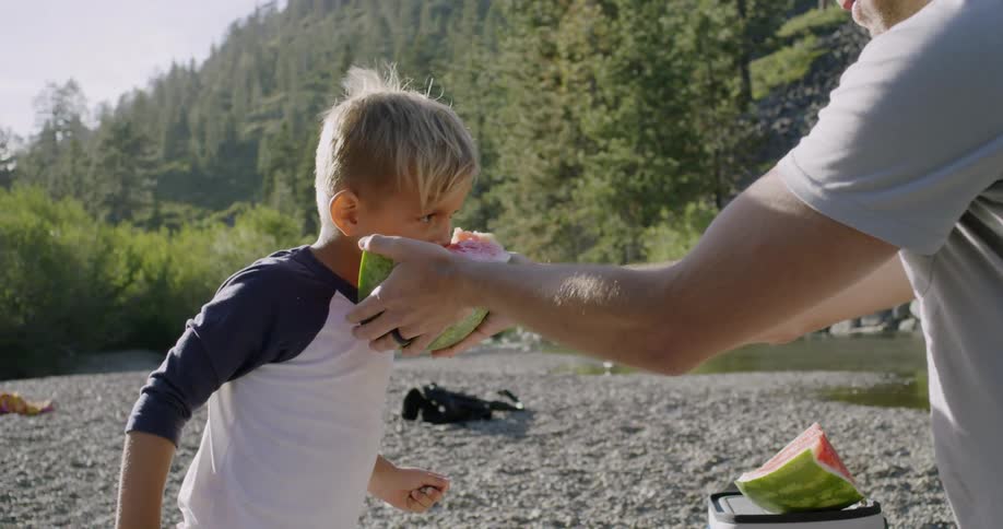 A man is giving a bite of watermelon to his young song