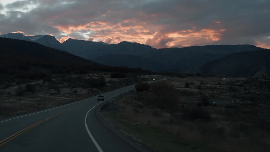 Cars traveling on mountain highway during cloudy sunset