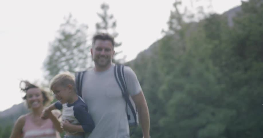 A dad runs while carrying his son and his wife runs alongside