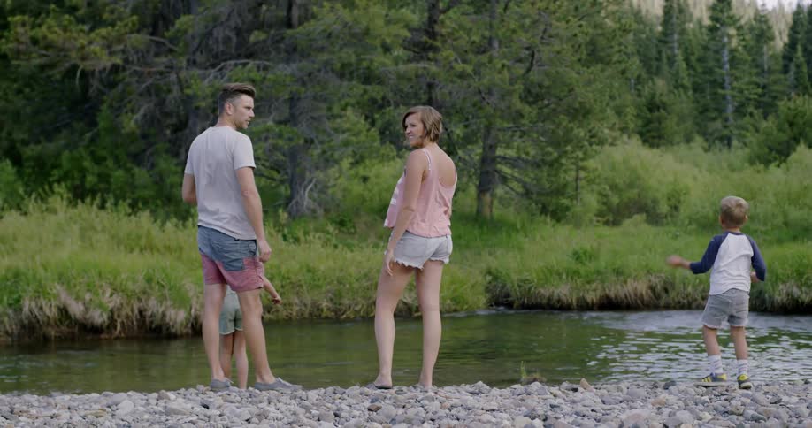Family stands and plays with rock next to river