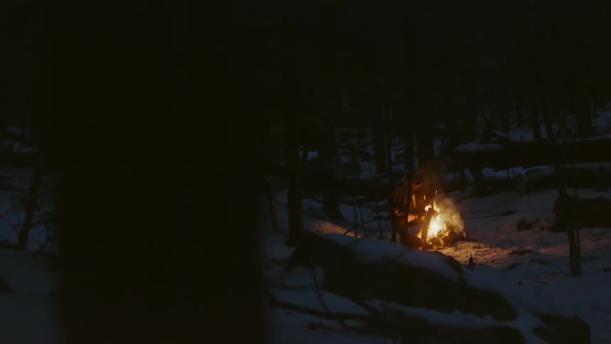 A man sits outside in the snow by a campfire