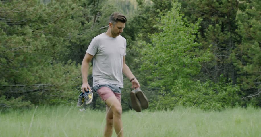 Man holding shoes is walking through grassy field