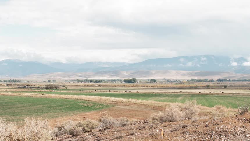 Clouds are hanging in the sky over farm fields in a valley