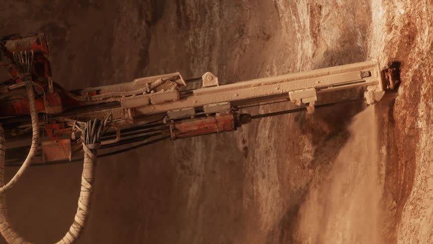A drill is boring into a rock wall in daylight