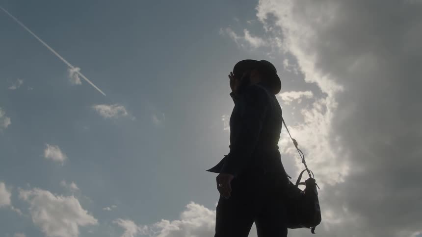 A man stands tipping up the brim of his hat as he looks around