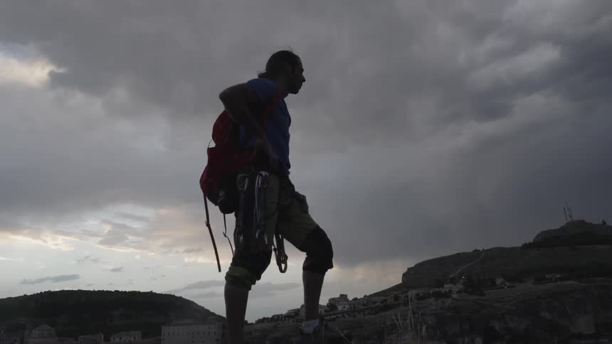 A man hiking beneath cloudy skies stops for a rest