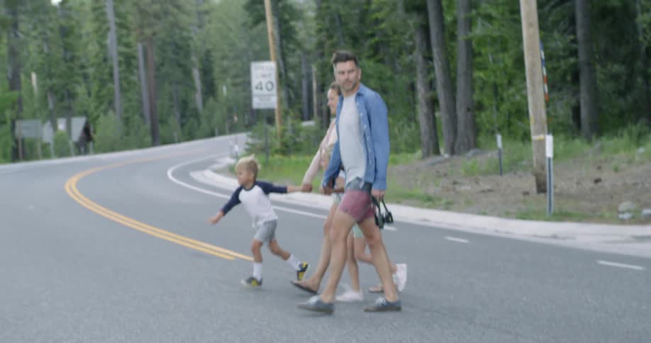 A family are crossing a road through a forest in daylight