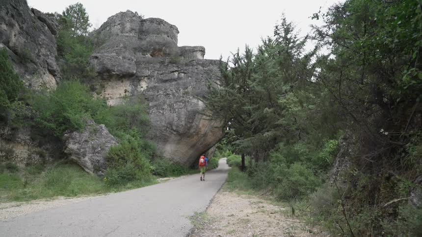 A man wearing a backpack walks a path under a rock