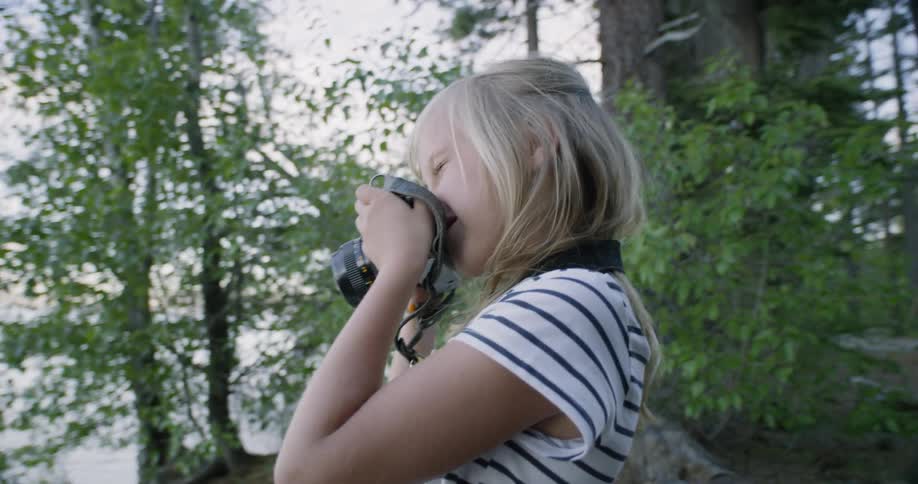 A girl smiles as she looks through the lens of a camera