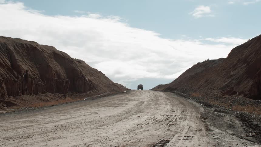 A dump truck travels over a hill on a dirt road
