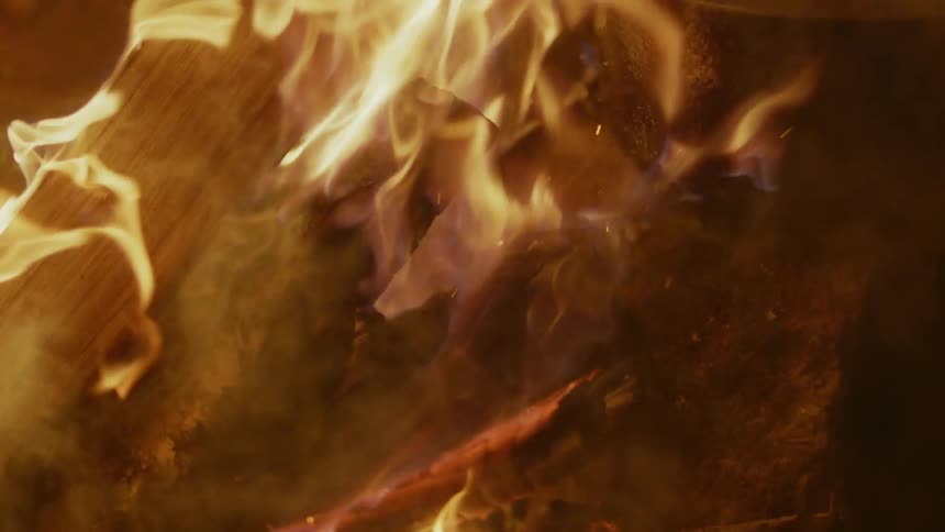 Flames are swirling around wood in a bonfire at night