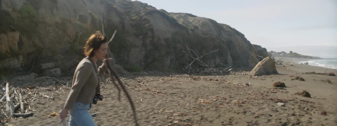 Woman with camera walks with stick on sandy beach